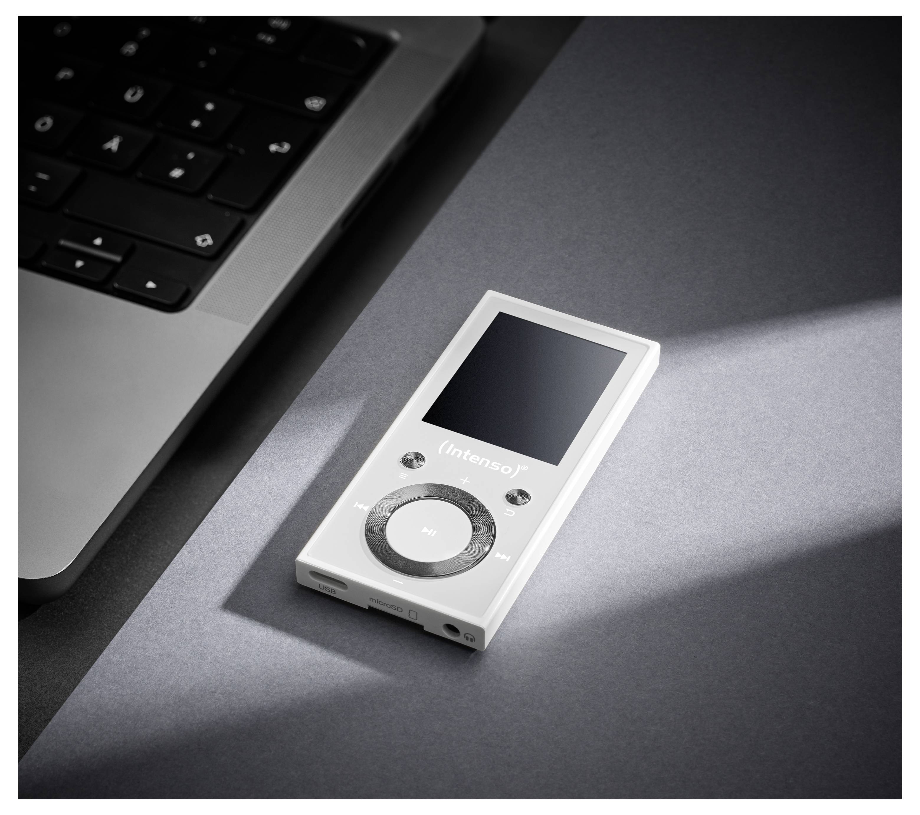 Ein silberner MP3-Player mit Bedienungstasten und einem kleinen Bildschirm liegt neben einer Laptop-Tastatur auf einem Schreibtisch, von Licht beleuchtet.