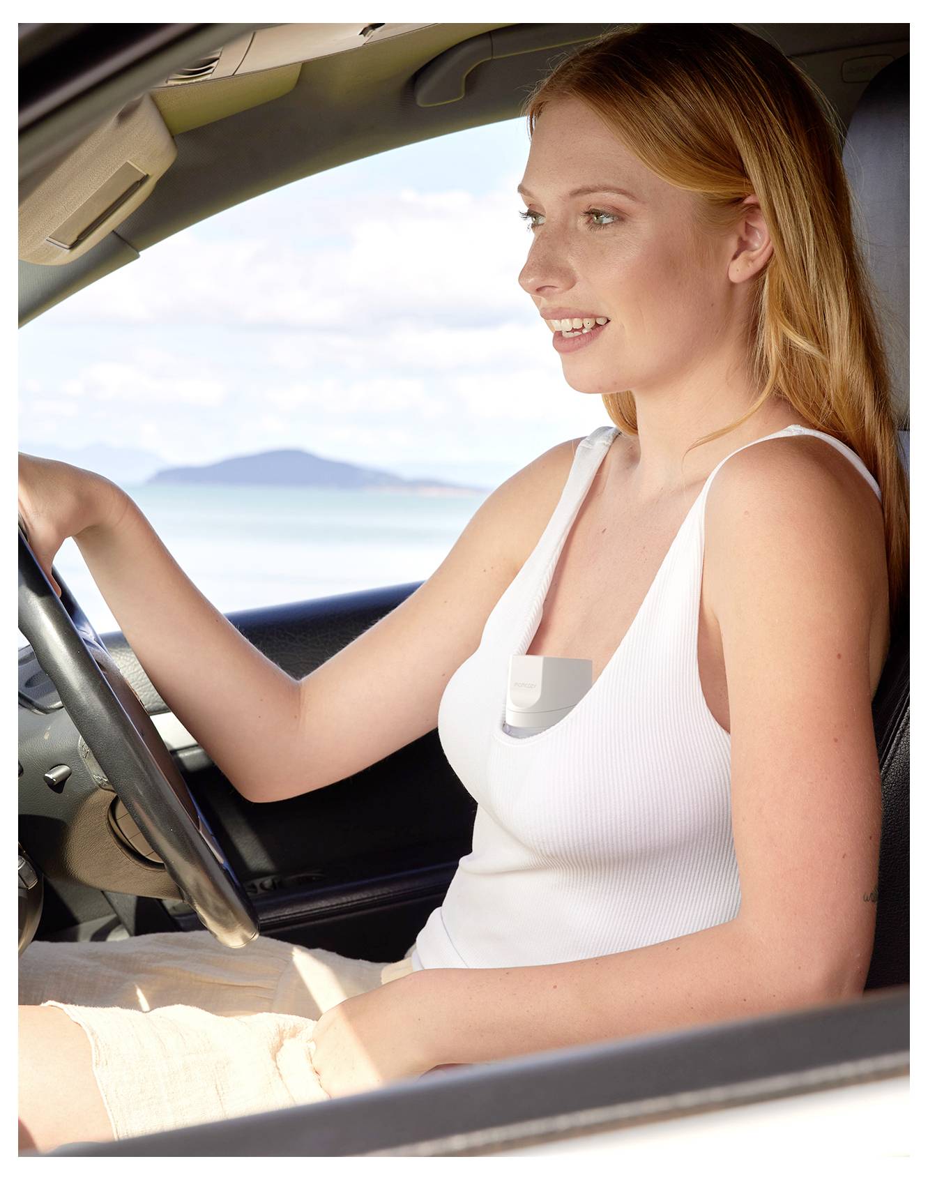 Eine Person sitzt in einem Auto am Meer, lächelt und schaut aus dem Fenster. Das Wageninnere und der Ozean sind sichtbar.
