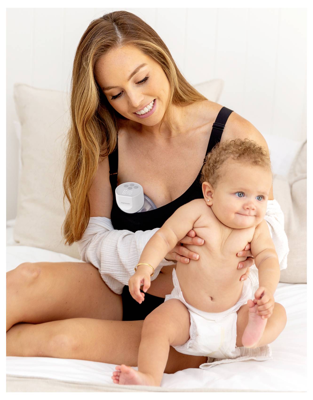 Eine Frau hält sanft ein lächelndes Baby in einer Windel auf einem Bett, offensichtlich in einem fürsorglichen und freudvollen Moment.