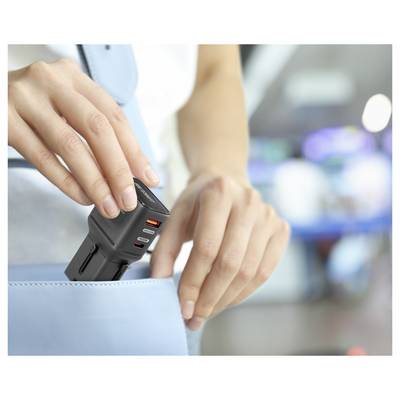 Eine Person legt einen kompakten schwarzen Mehrfach-Stromadapter mit USB-Anschlüssen in eine hellblaue Handtasche, was Tragbarkeit und Komfort suggeriert.