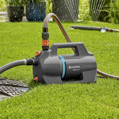 Eine Gartenschlauchrolle mit einem leuchtend orangefarbenen Griff auf einem grünen Rasen, mit sprudelndem Wasser im Hintergrund.