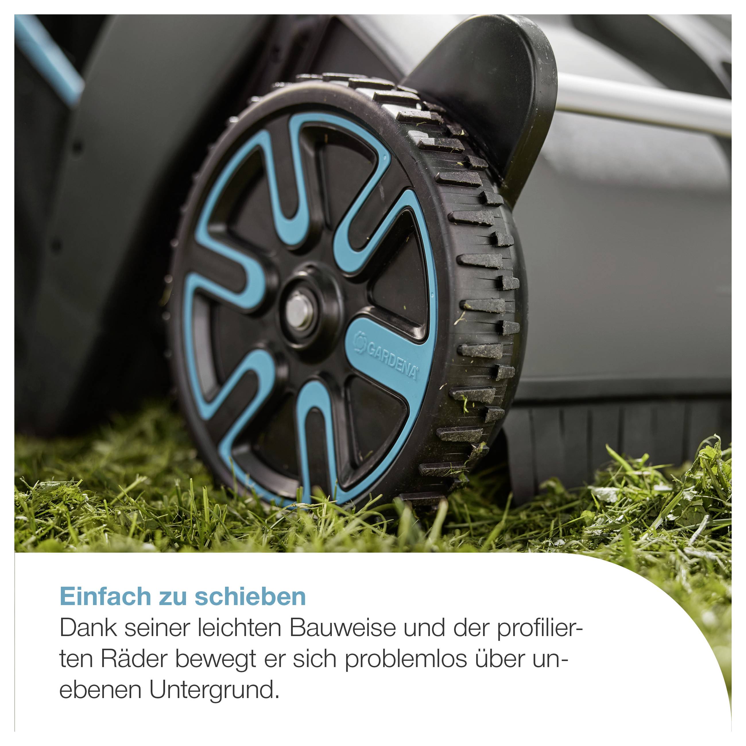Nahaufnahme eines Rasenmähers mit großem Profilrad auf Gras; Text erklärt: 'Einfach zu schieben' dank leichter Bauweise und Rädern für unebenen Untergrund.