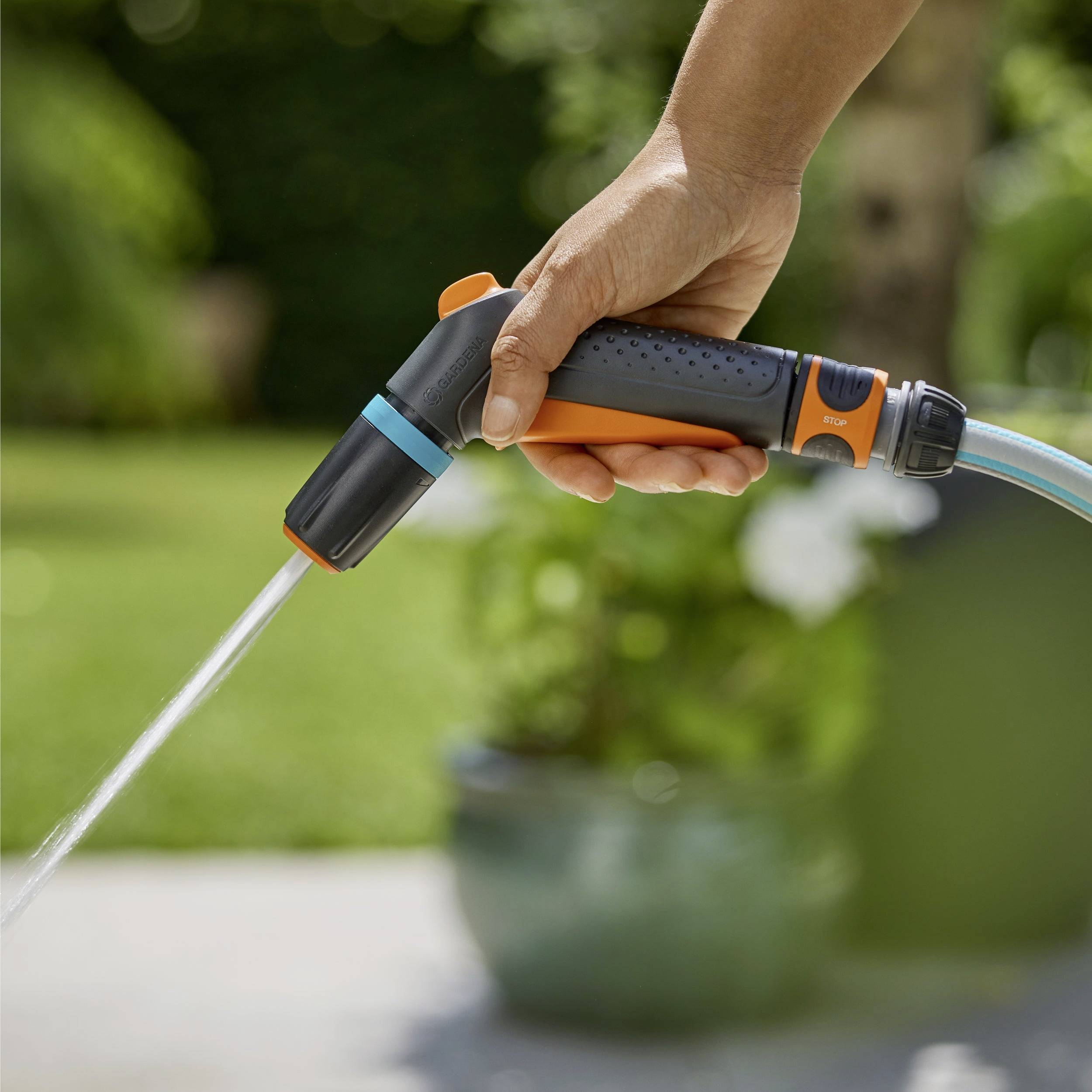 Eine Nahaufnahme einer Hand, die eine Gartenschlauchbrause hält und einen Garten mit einem sanften Sprühregen bewässert, mit unscharfen grünen Blättern im Hintergrund.