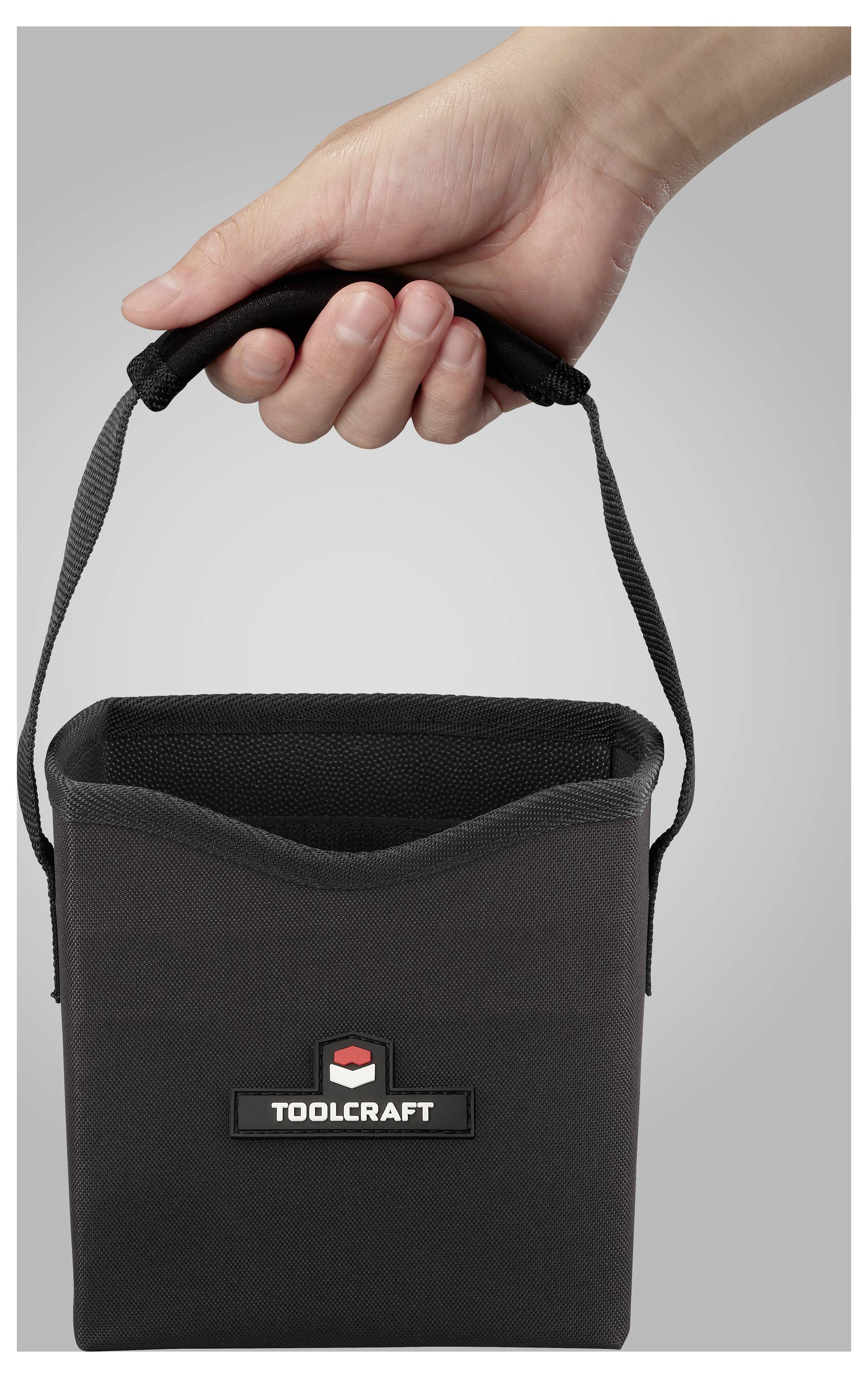 Eine Hand hält eine schwarze Toolcraft-Tasche mit Griff. Die Tasche ist rechteckig und oben offen, mit dem Markenlogo auf der Seite.