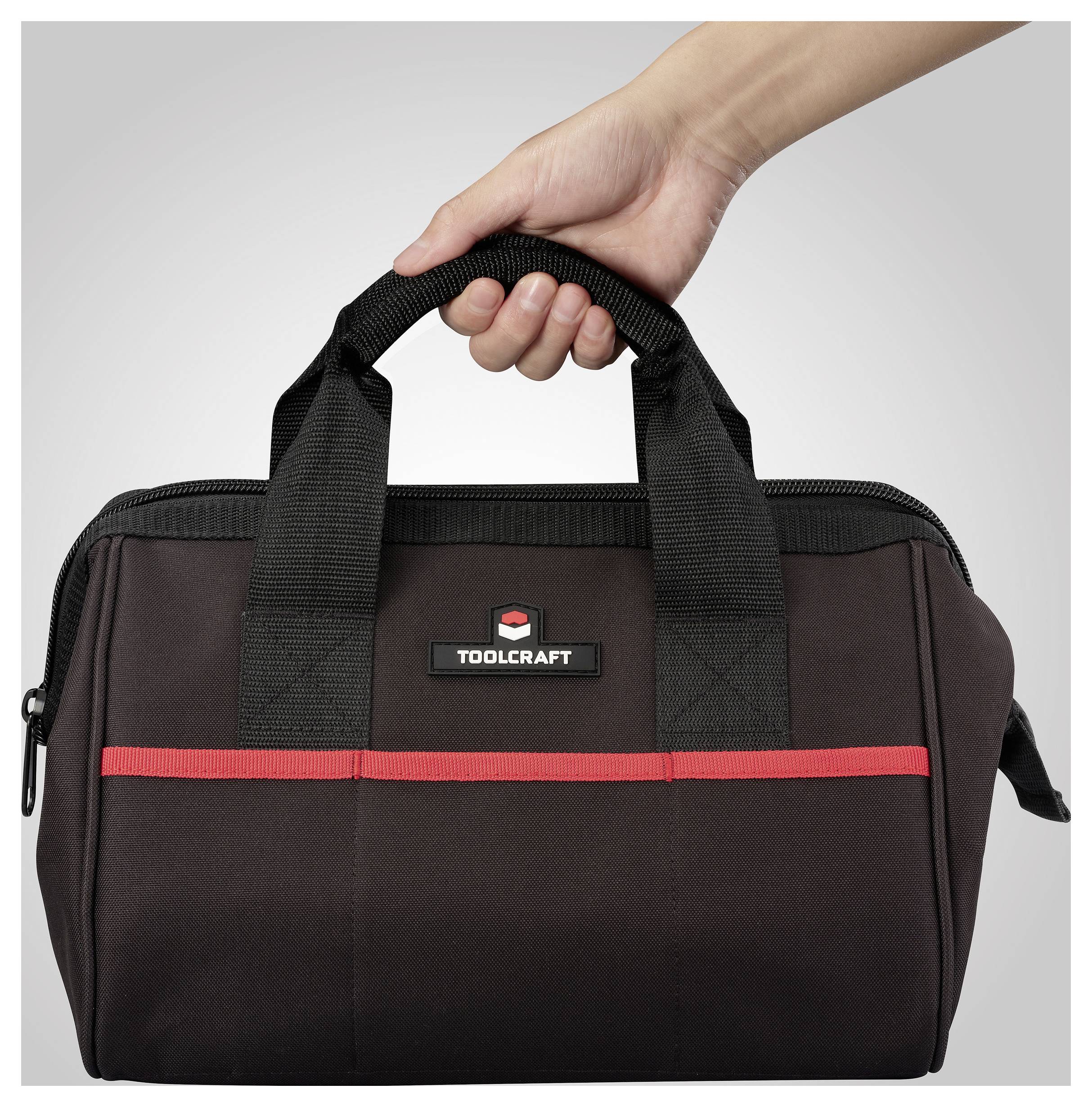 Eine Hand hält eine schwarze und rote Werkzeugtasche mit der Aufschrift „TOOLCRAFT".