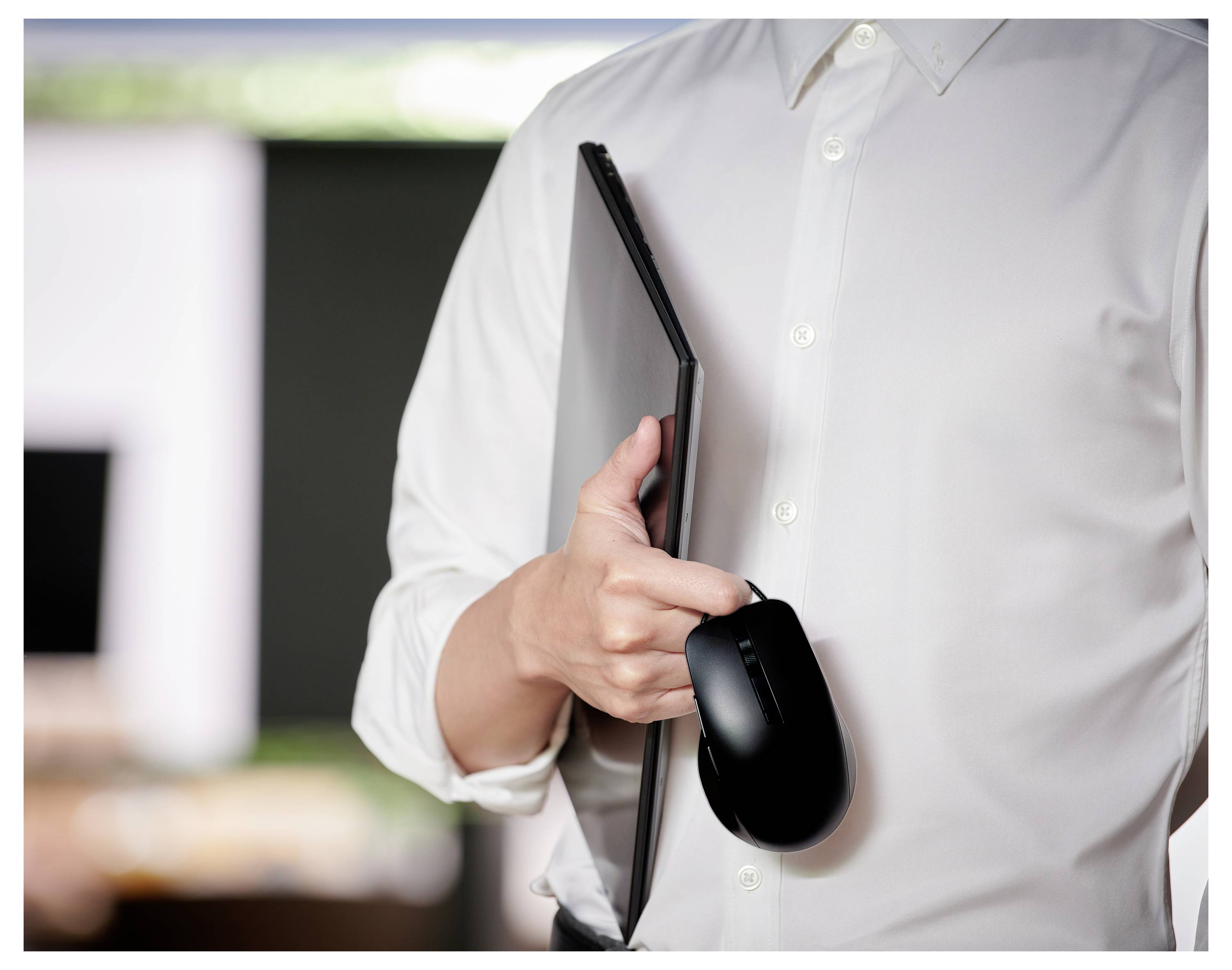 Eine Person in einem weißen Hemd, die einen geschlossenen Laptop und eine Computermaus hält und sich drinnen befindet.