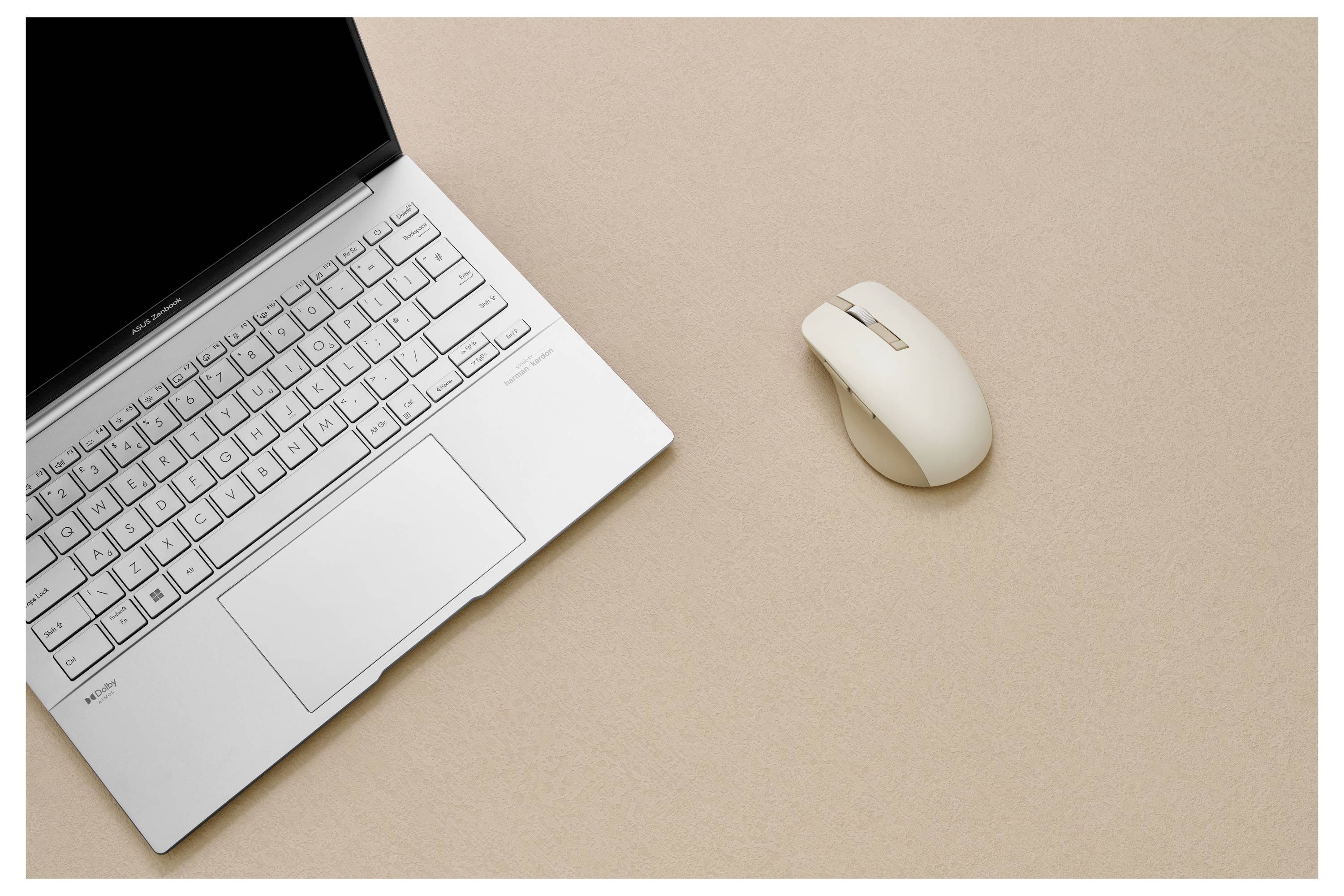 Ein silberner Laptop mit sichtbarer Tastatur und Trackpad ist auf einer beigen Oberfläche geöffnet, daneben liegt eine kabellose Maus.