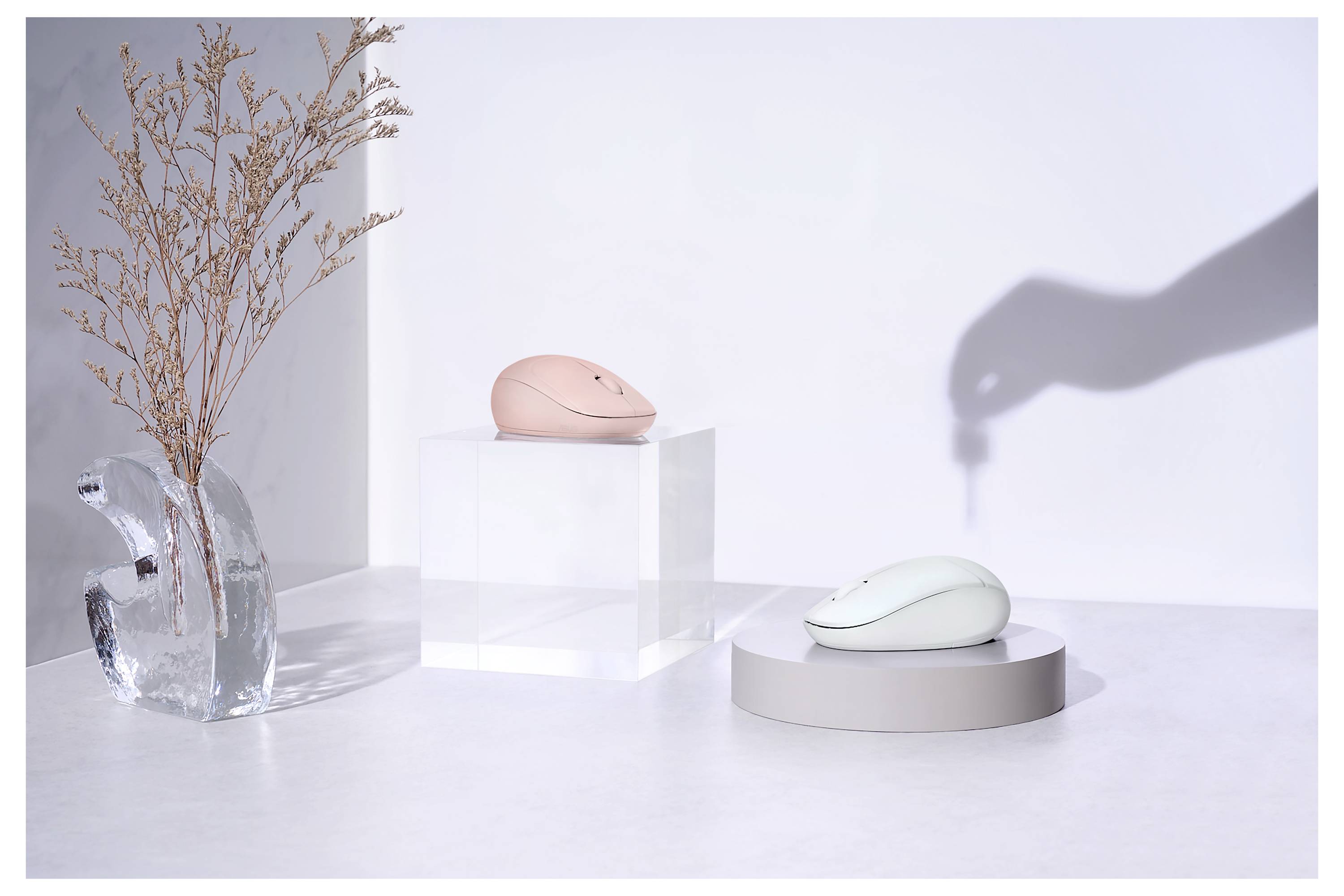 Eine minimalistische Anordnung mit zwei Computermäusen, die auf weißen Plattformen präsentiert werden; eine ist pink, die andere weiß. Ein Handschatten zeigt auf die Mäuse.