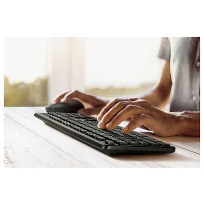 Eine Person, die auf einer drahtlosen Tastatur tippt, mit einer Maus in der Nähe, in einem hellen Raum mit Fensterblick.