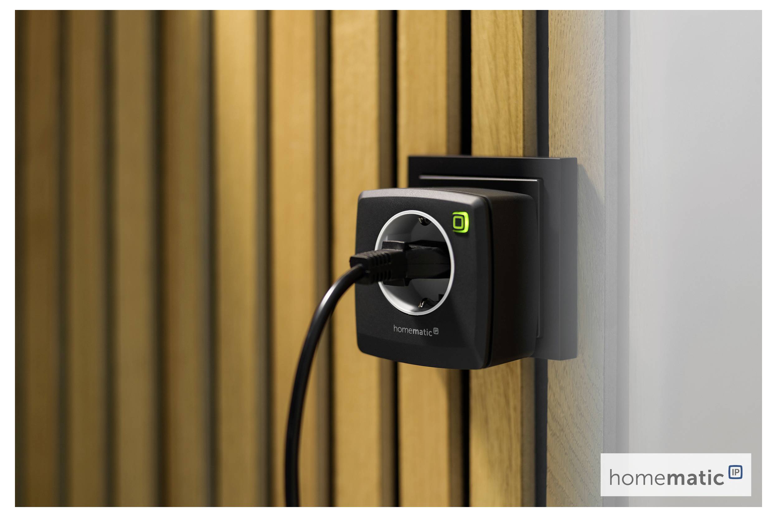 Eine Smart-Steckdose, die an einer Holzwand installiert ist, mit einem Gerät, das in sie eingesteckt ist; ein Logo von "homematic IP" ist auf der Steckdose sichtbar.