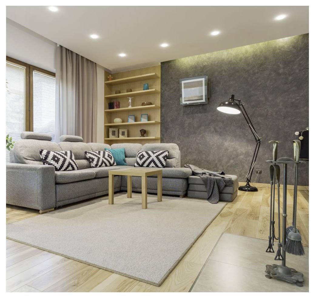 Ein modernes Wohnzimmer mit einem grauen Sofa, geometrischen Kissen, einer Stehlampe, Holzregalen und einem hellen Teppich auf Holzdielen.