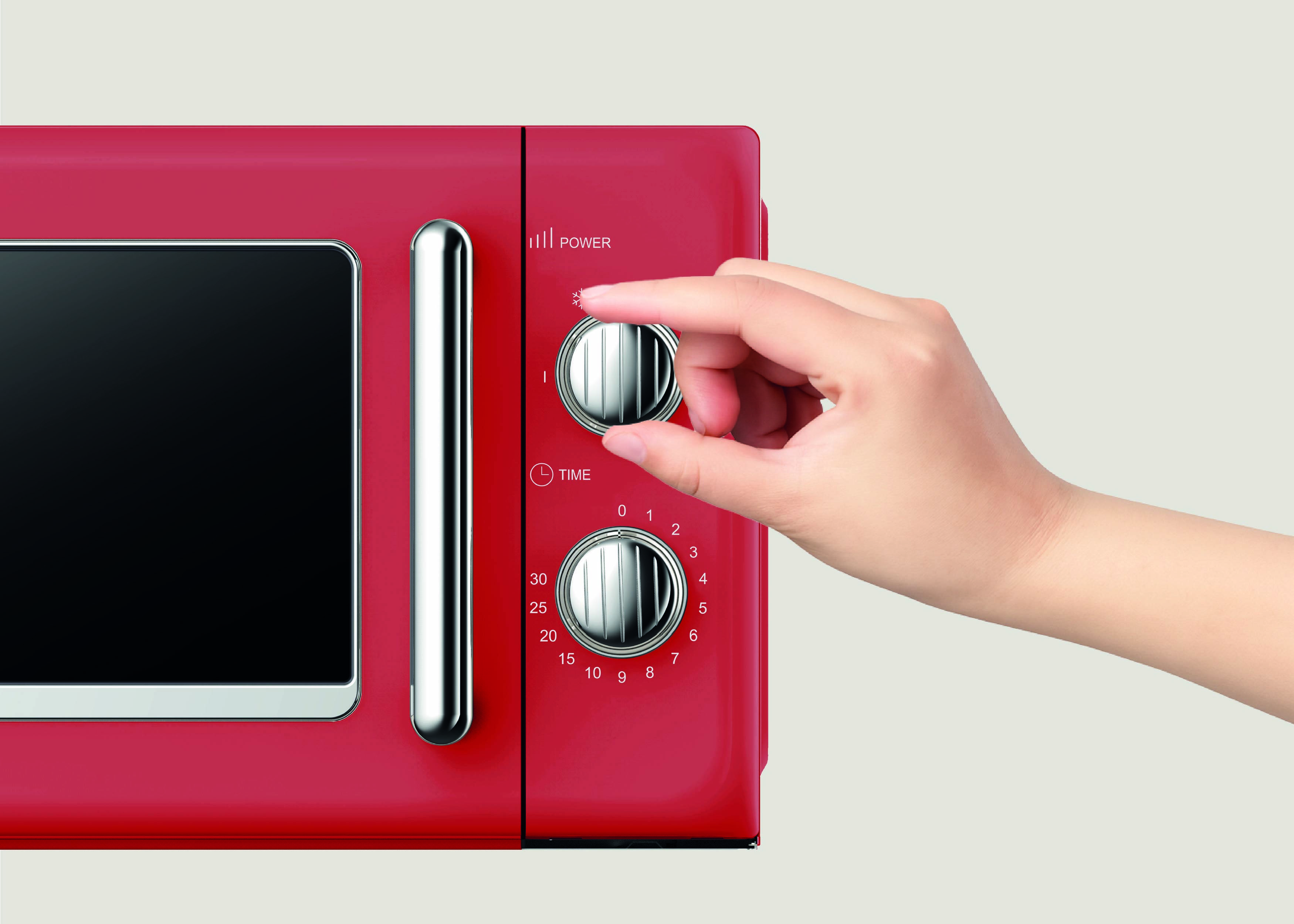 Eine Hand justiert den Zeiteinstellungsregler an einem roten Mikrowellenherd, wobei die Leistungseinstellung in der Nähe sichtbar ist.