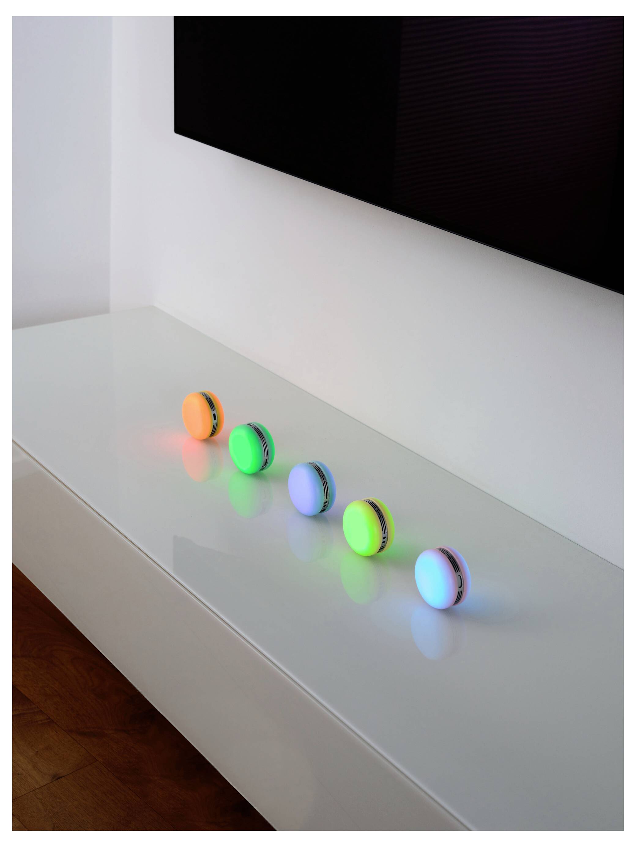 Fünf bunte, runde Lichter auf einer weißen Oberfläche, die jeweils ein anderes farbiges Leuchten erzeugen: orange, grün, blau und lila.