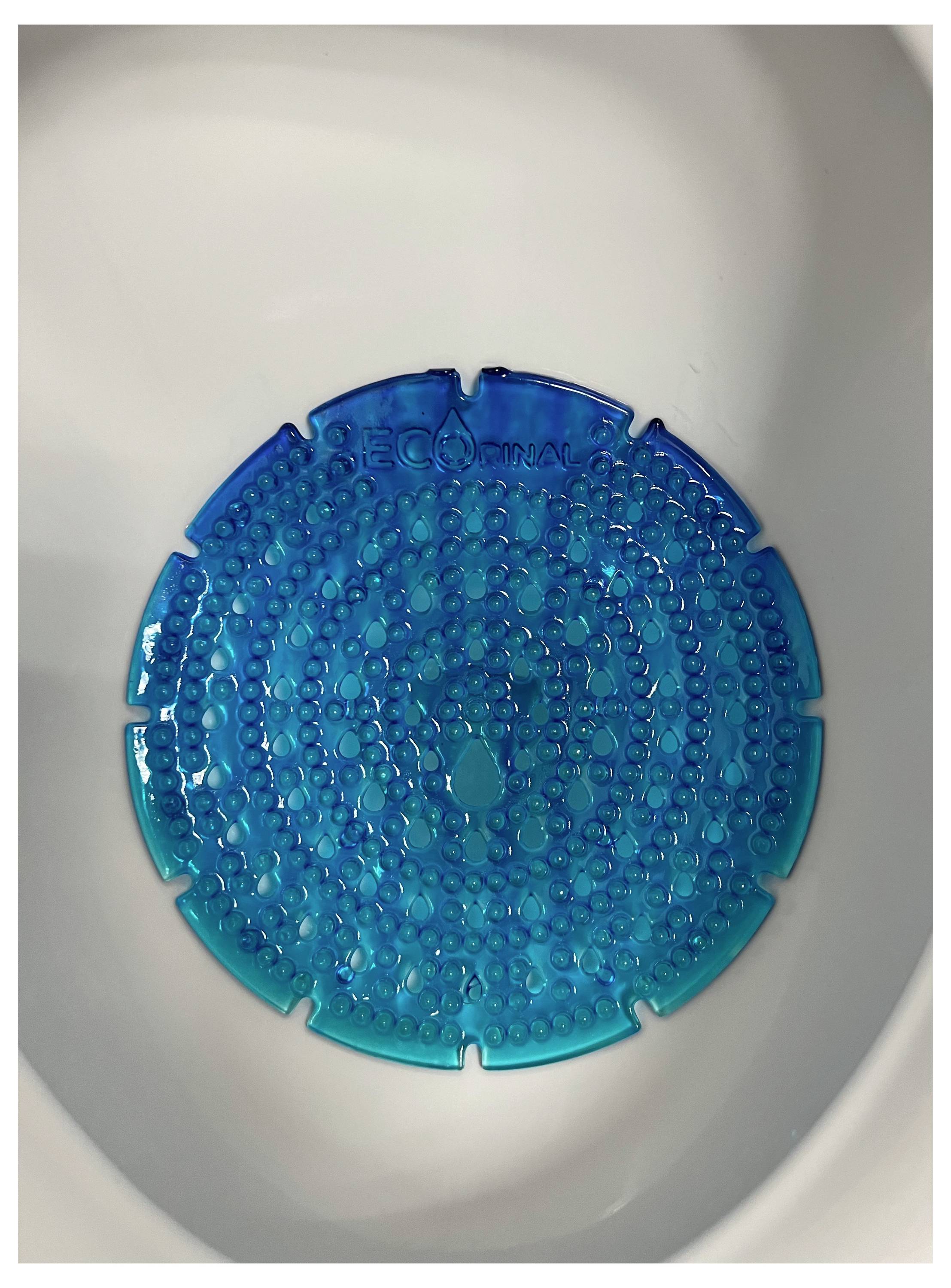 Ein blauer, kreisförmiger Urinalsieb mit strukturierter Oberfläche wird in ein weißes Urinal eingelegt, um Geruch und Hygiene zu kontrollieren.