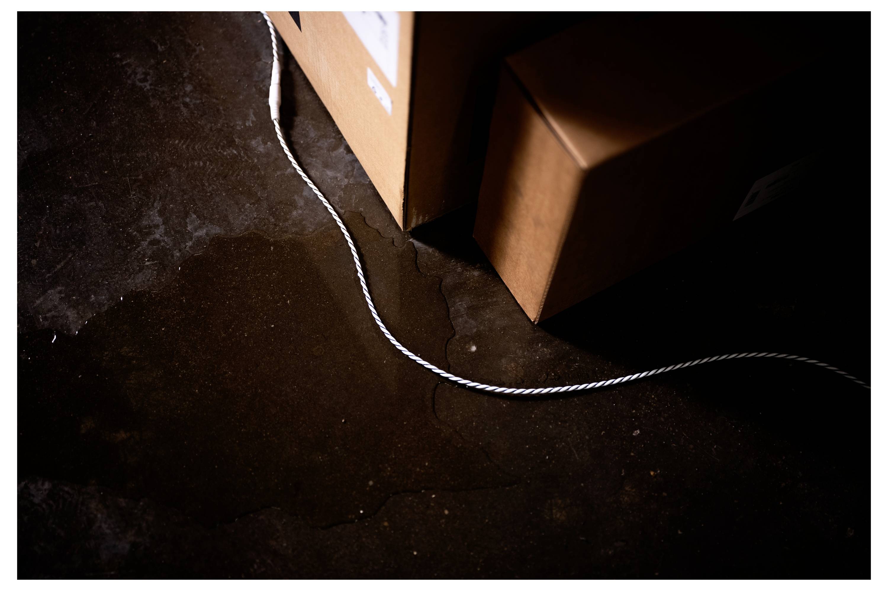 Nasser Boden in der Nähe von Kartons und einem Seil deutet auf eine mögliche Gefahrenquelle in einem Innenraum hin und weist auf die Notwendigkeit von Vorsicht hin.