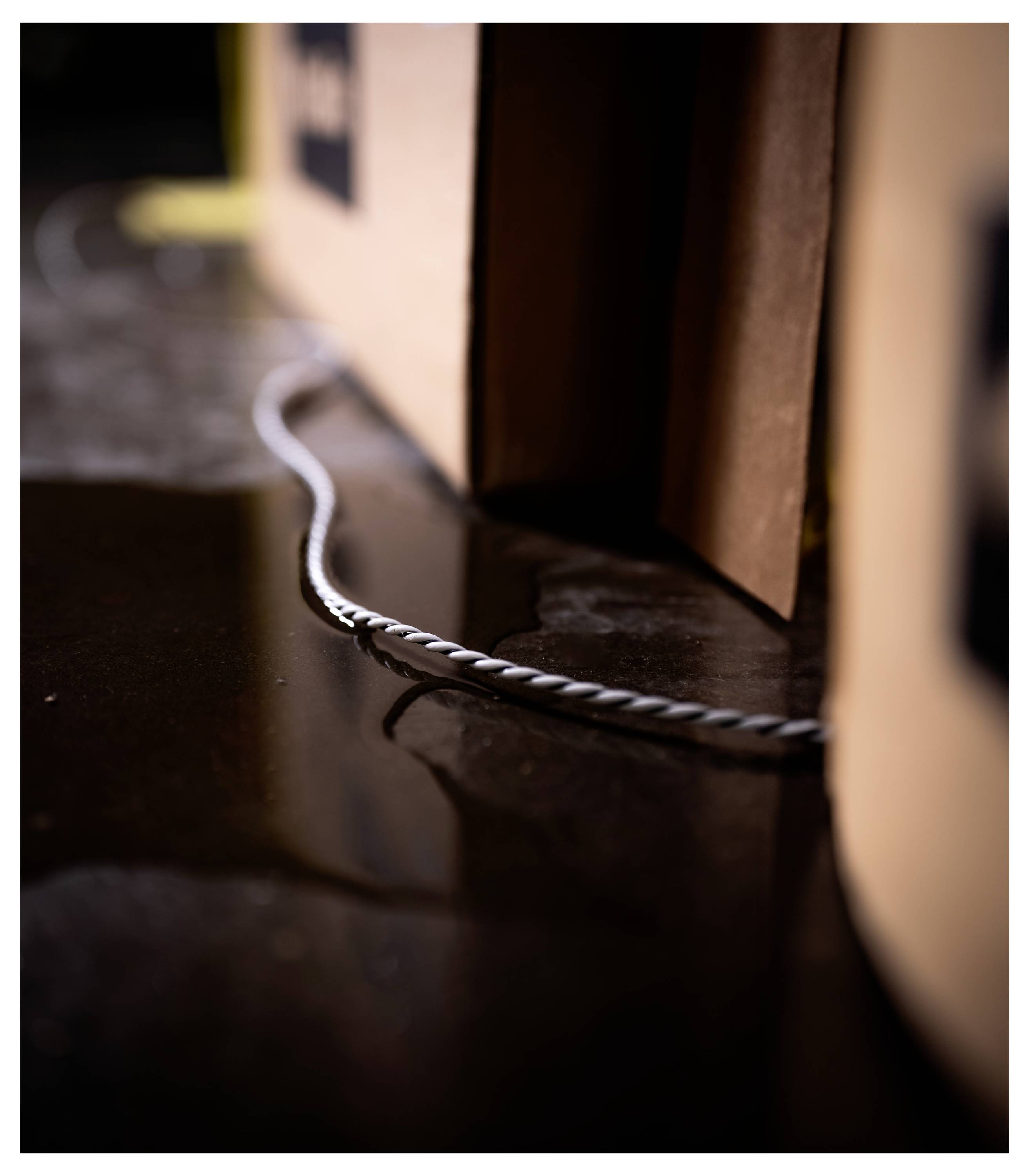Eine Pappschachtel auf einer nassen, reflektierenden Oberfläche, mit einem dünnen, verdrehten Kabel, das von unter dem Rand der Schachtel herausragt.