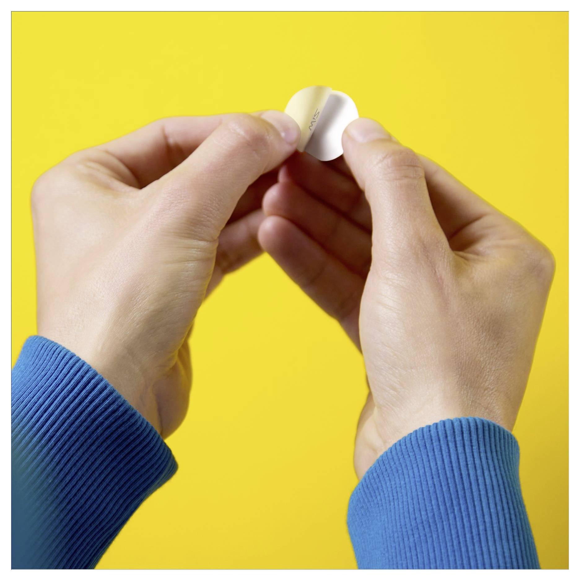 Hände, die eine runde Klebeetikette mit gelbem Hintergrund abziehen. Die Person trägt ein blaues langärmliges Hemd.