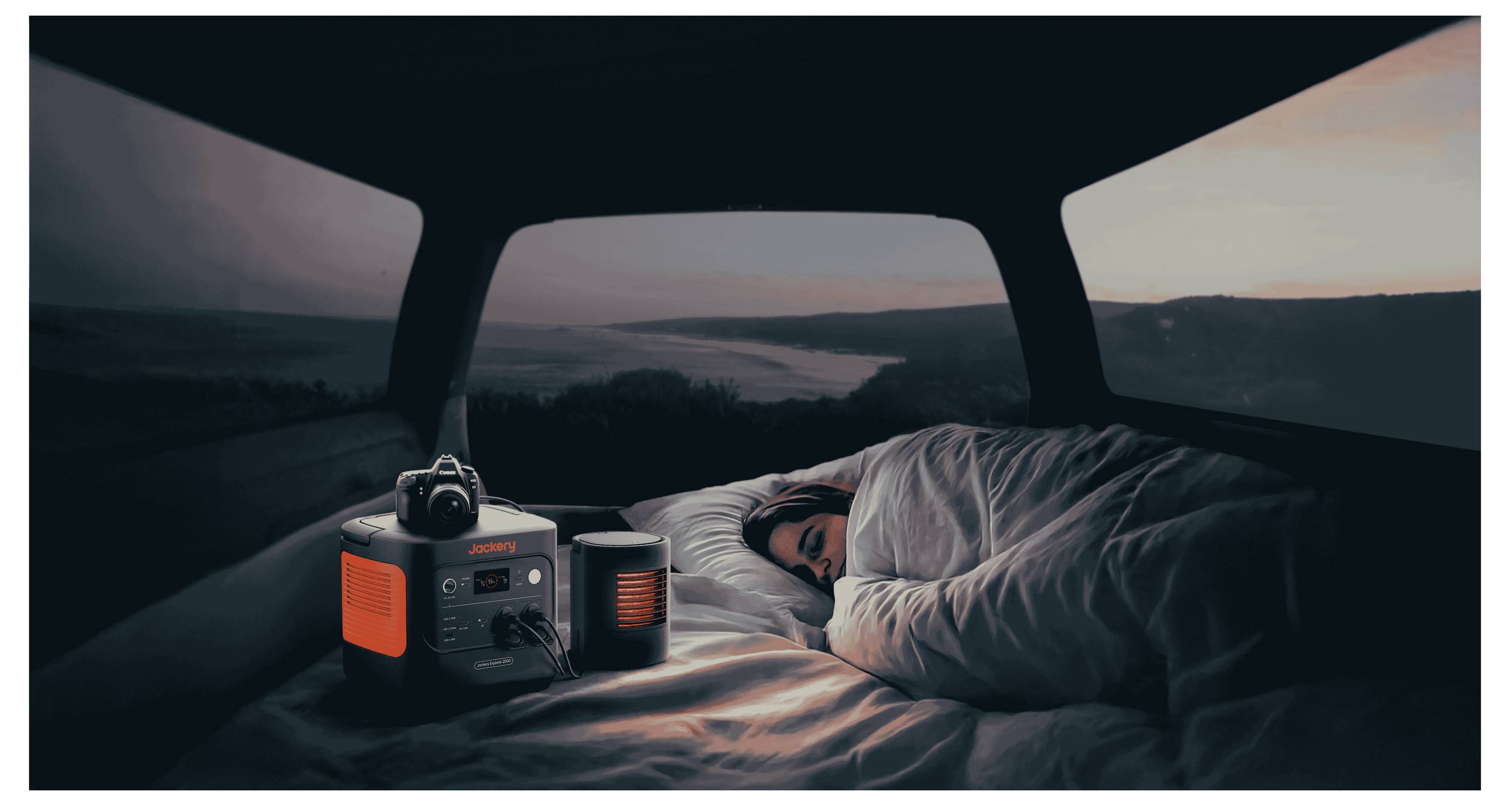 Eine Person schläft bei Morgendämmerung in einem Fahrzeug, umgeben von Decken. Ein tragbares Stromaggregat und Lampen befinden sich in der Nähe und deuten auf Camping oder Reisen hin.