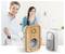 Ein lächelndes Paar steht in einem hell erleuchteten Raum hinter zwei Smart-Home-Geräten, einem digitalen Stecker und einer Türklingel, die im Vordergrund platziert sind.