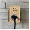 Ein Smart-Stecker im Holz-Design, der an einer grauen gefliesten Wand montiert ist, mit einem schwarzen Kabel, das in seine Buchse gesteckt ist und ein Stromicon zeigt.