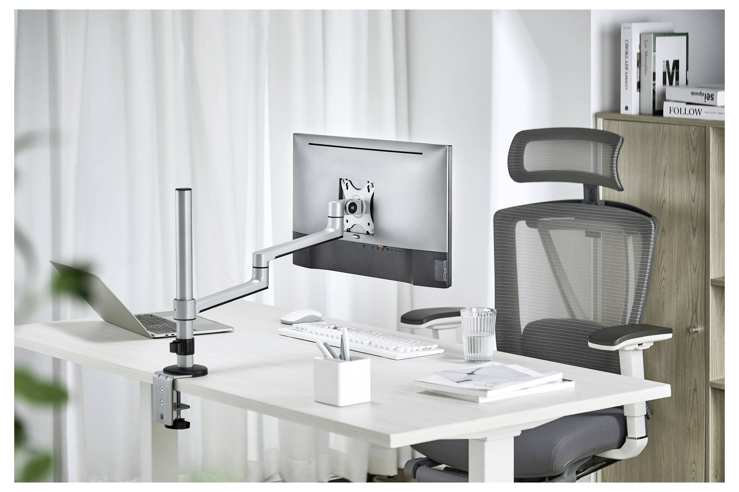 Ein ergonomisches Büro-Setup mit einem Monitor auf einem verstellbaren Arm, Tastatur, Maus und einem Mesh-Stuhl in einem hellen, ordentlichen Arbeitsbereich.