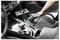 Autoinnenraum absaugen: Hand mit kleinem Staubsauger auf schwarzem Sitz, in der Nähe der Schaltkulisse und der Autobatterie.