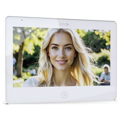Eine Person mit langem blondem Haar lächelt im Freien, mit Bäumen und Sonnenlicht im Hintergrund. Eine andere Person sitzt in der Ferne.
