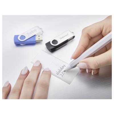 Eine Hand schreibt „Holiday 2020" auf ein Etikett, während zwei USB-Laufwerke mit den Beschriftungen „Backup" und „Intenso" auf dem Tisch liegen.