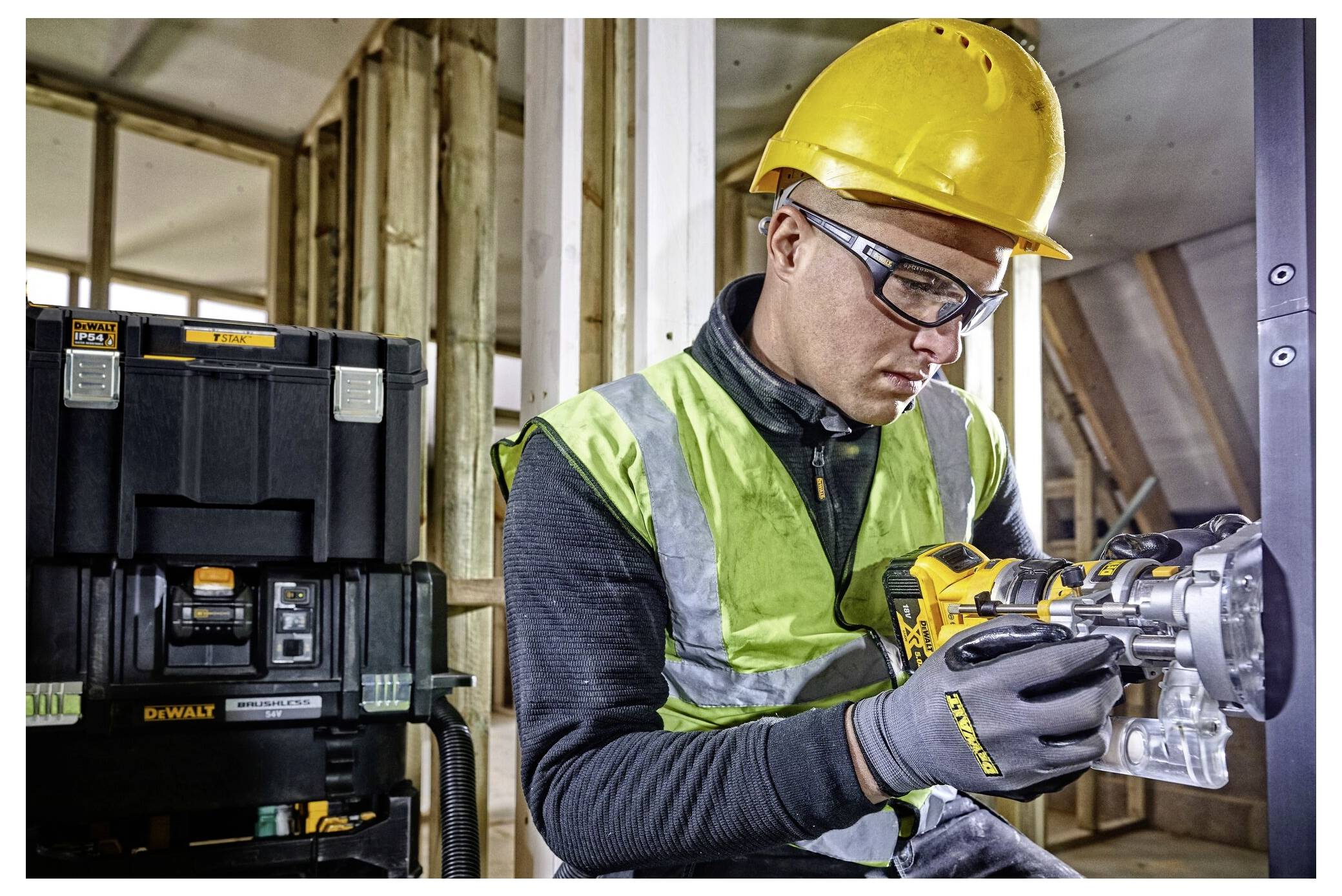 Ein Bauarbeiter in Schutzausrüstung bedient ein Elektrowerkzeug in einem teilweise fertiggestellten Holzbauwerk, mit Ausrüstung im Hintergrund.