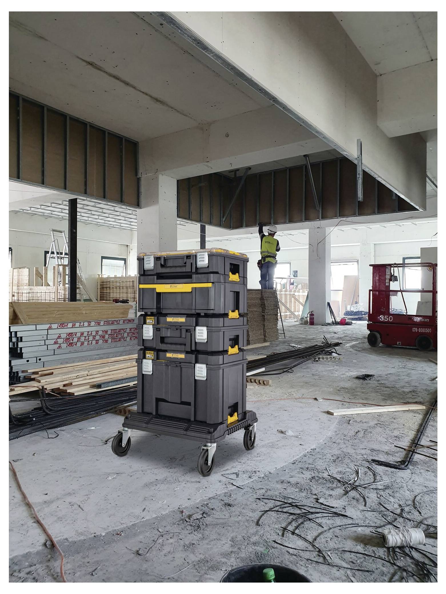 Eine Baustelle mit einem Arbeiter auf Gerüsten und einem Stapel von Werkzeugkisten auf Rädern im Vordergrund, umgeben von Baumaterialien.