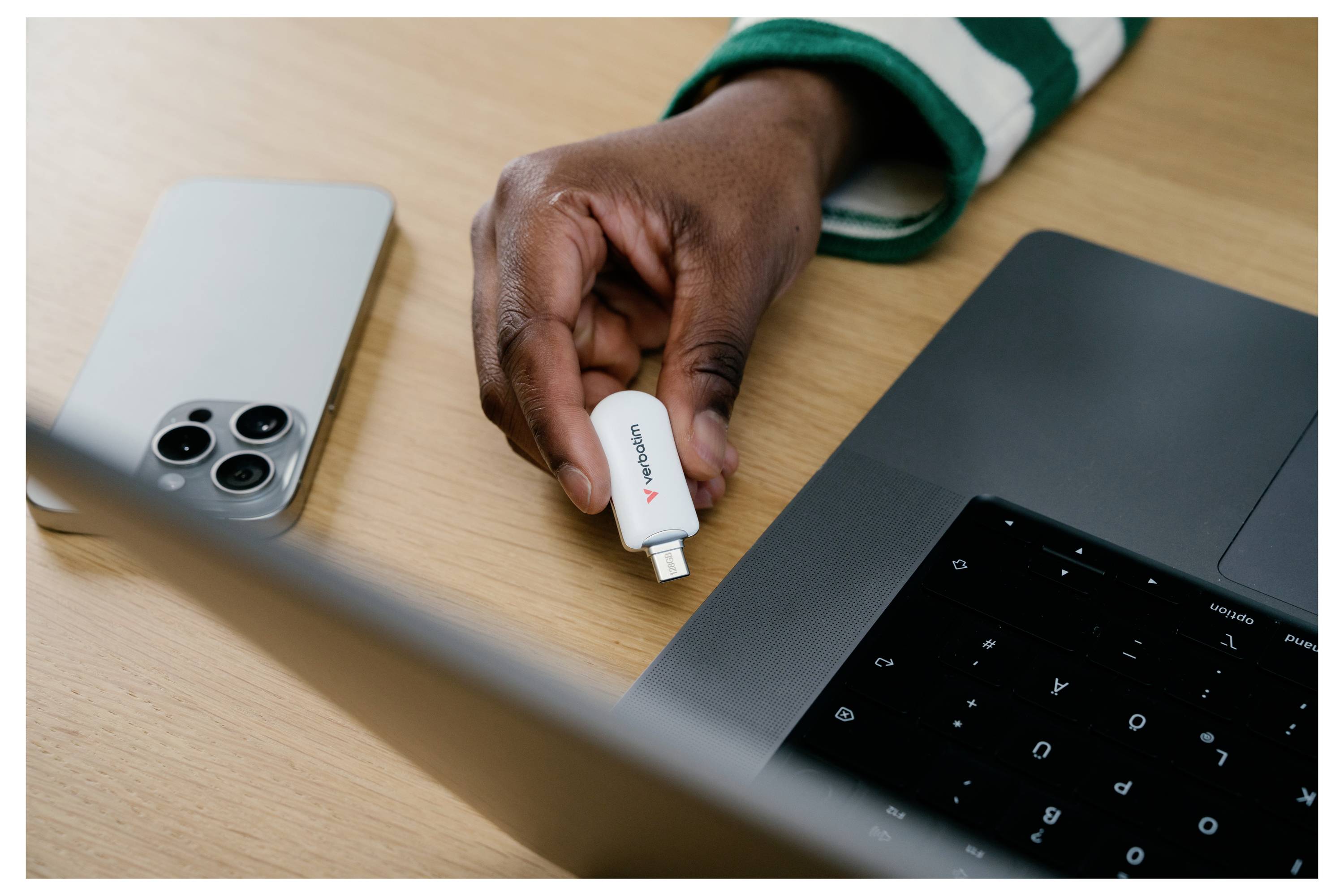 Hand fügt einen kleinen weißen USB-C-Adapter neben einem Laptop und Smartphone auf einem Schreibtisch ein und deutet auf Gerätekonnektivität oder Datentransfer hin.