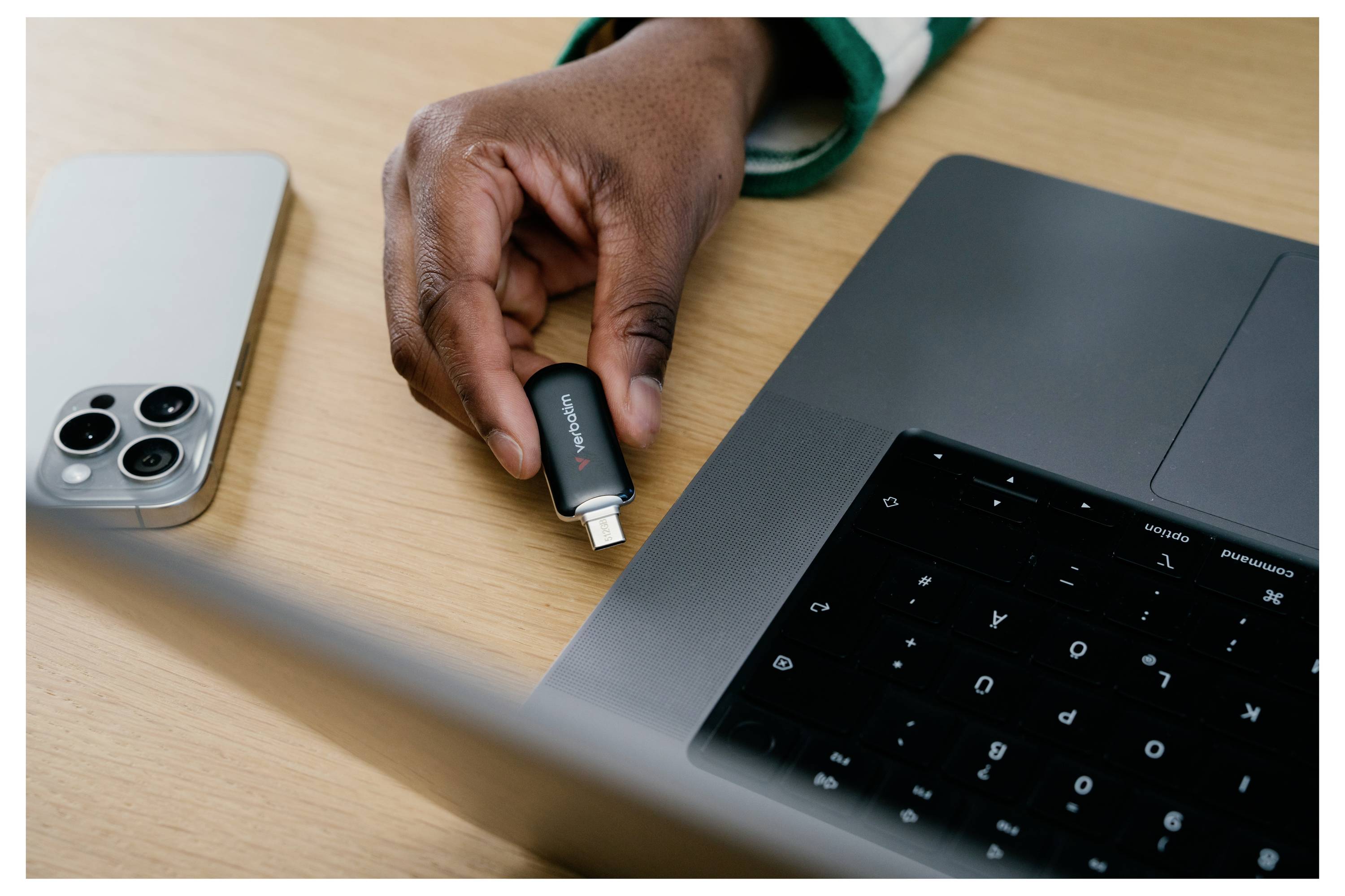 Hand, die einen USB-C-Adapter in einen Laptop neben einem Smartphone auf einem Schreibtisch einsteckt.
