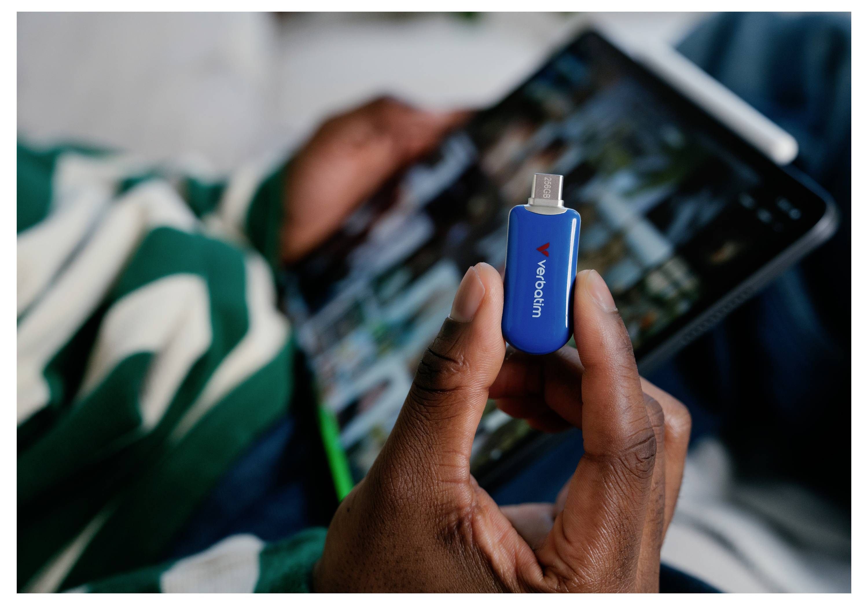 Eine Hand, die einen blauen Xvodan USB-Stick vor einem unscharfen Tablet-Bildschirm hält.