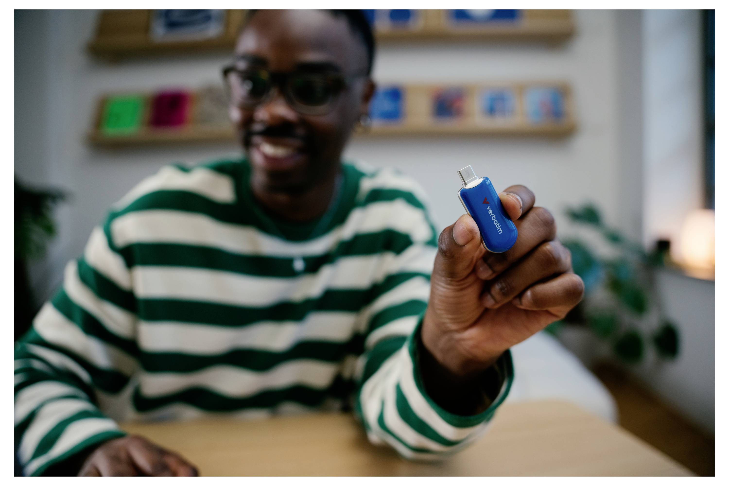 Lächelnder Mann im gestreiften Hemd hält einen blauen USB-Stick zur Kamera hoch.