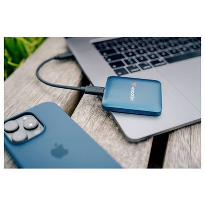 Externe blaue Verbatim-SSD, die über USB-C mit einem Laptop auf einem Holztisch verbunden ist, mit einem blauen iPhone im Vordergrund.