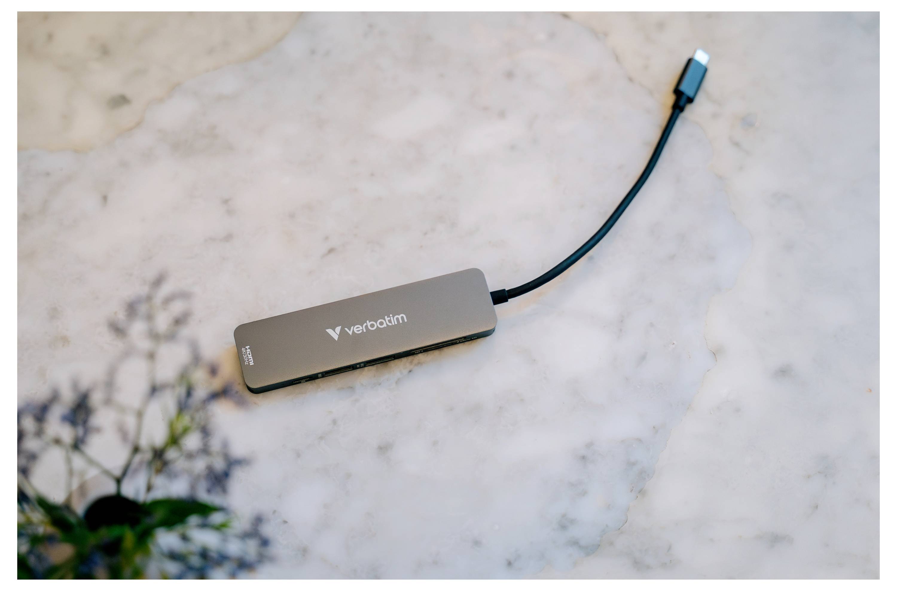 Ein Verbatim USB-C-Hub ruht auf einer Marmoroberfläche, wobei sein angeschlossenes Kabel in einem blauen USB-Stecker endet.