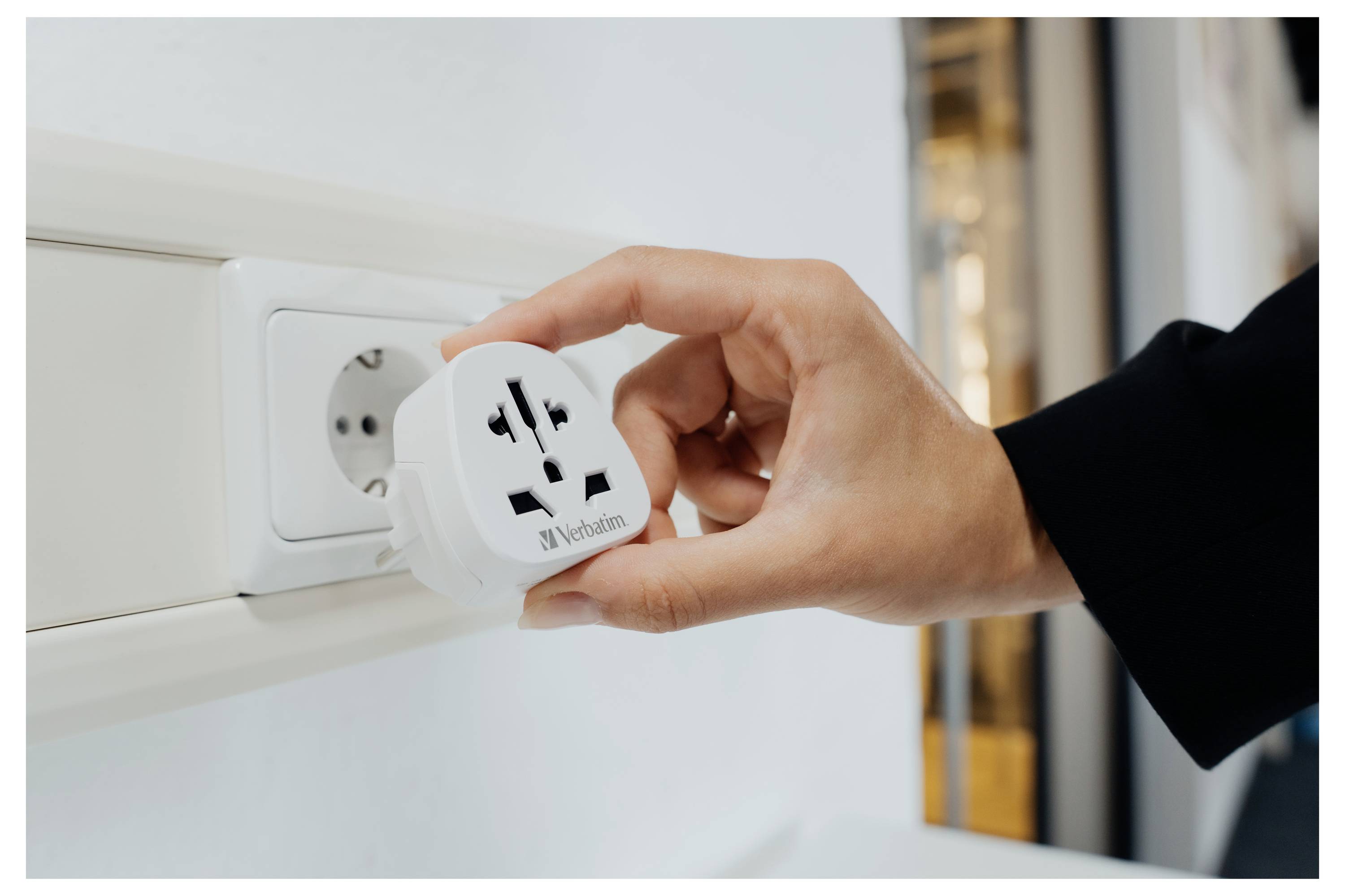 Hand, die einen universellen Reiseadapter in eine Wandsteckdose in einem Zimmer einsteckt.