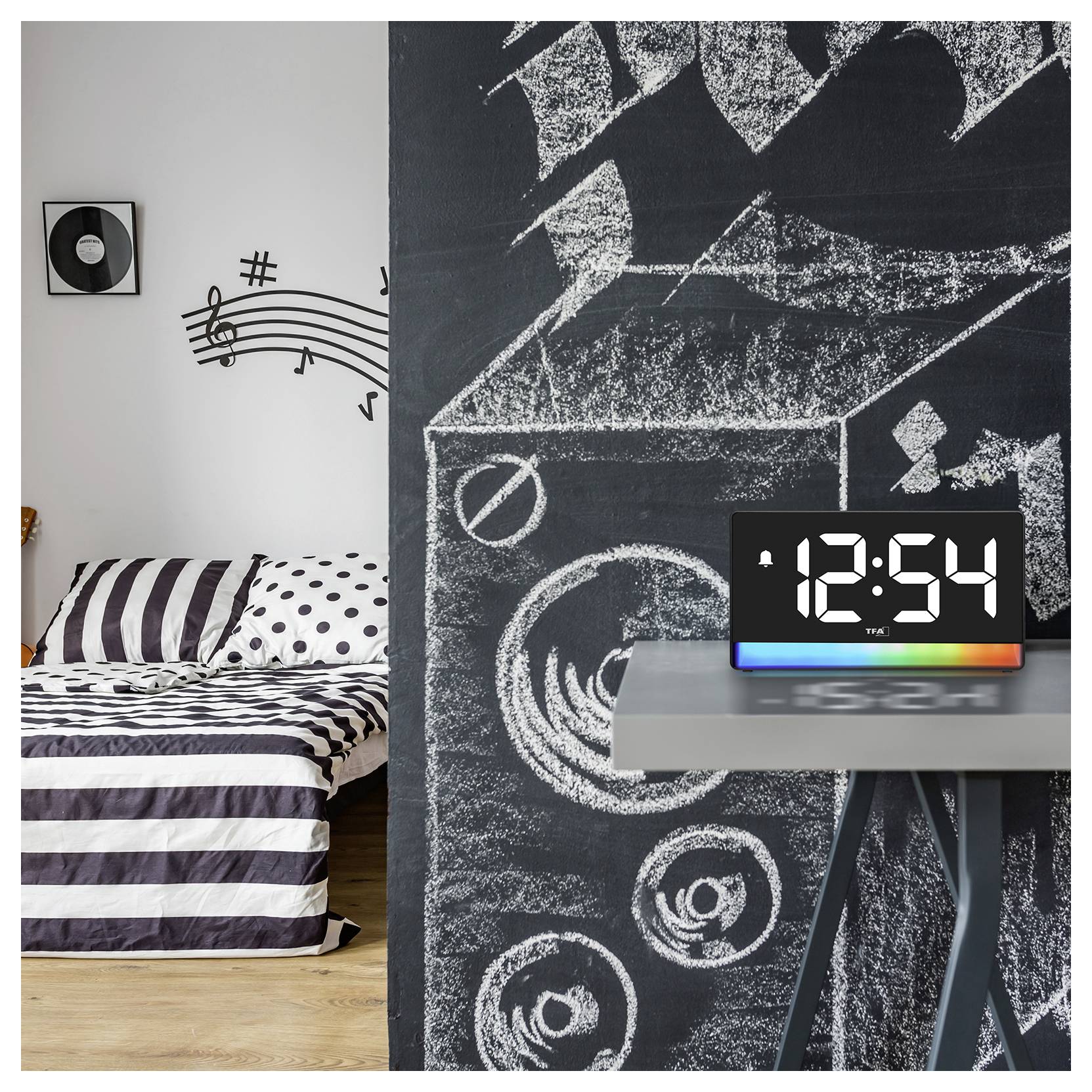 Ein Schlafzimmer mit einem gestreiften Bett und einer Tafelwand mit Musiknoten und Zeichnungen von Lautsprechern. Eine digitale Uhr auf einem Tisch zeigt '12:54'.