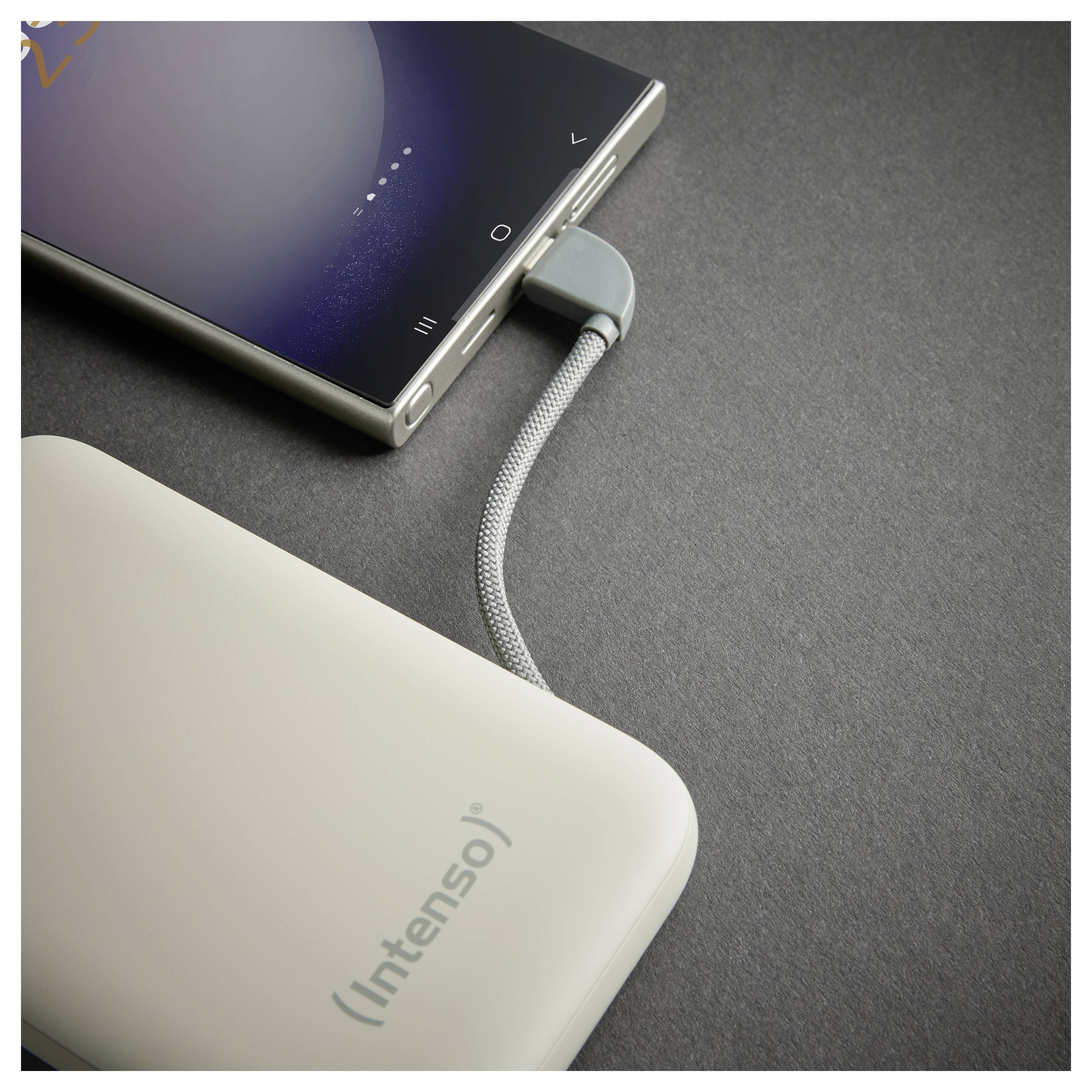 Ein Smartphone, das über ein geflochtenes USB-Kabel mit einer Powerbank verbunden ist, liegt auf einer dunklen Oberfläche; die Powerbank ist mit „Intenso" gekennzeichnet.