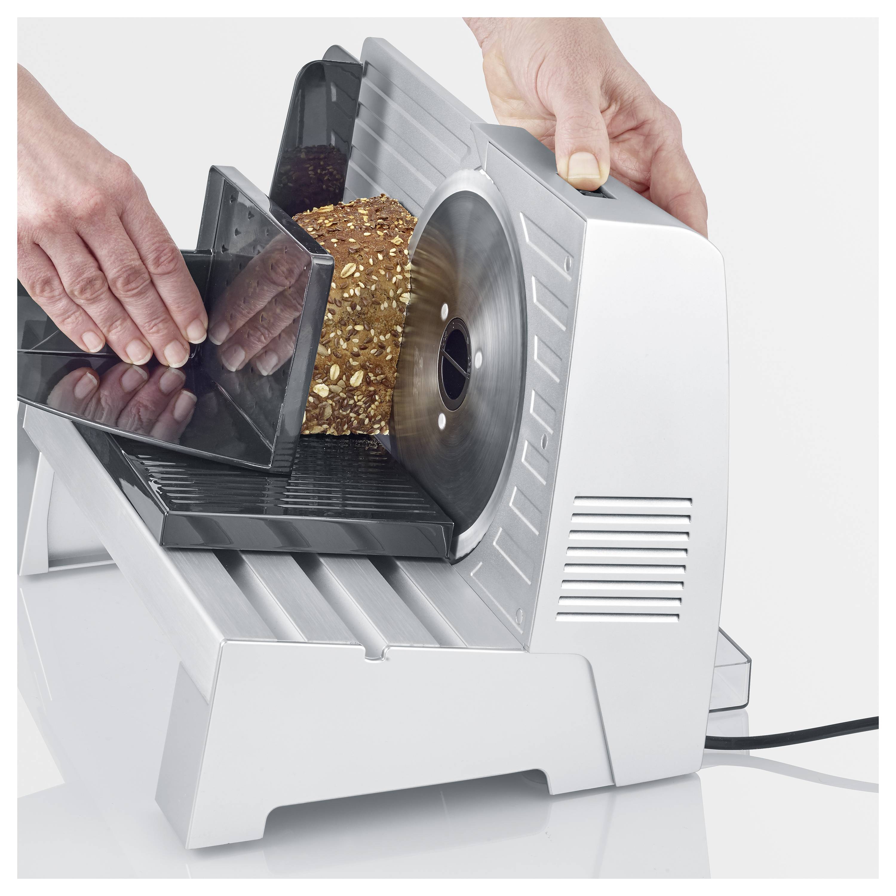 Eine Person schneidet einen Laib Mehrkornbrot mit einem elektrischen Schneidegerät, wodurch die Fähigkeit des Geräts demonstriert wird, Brot gleichmäßig zu schneiden.