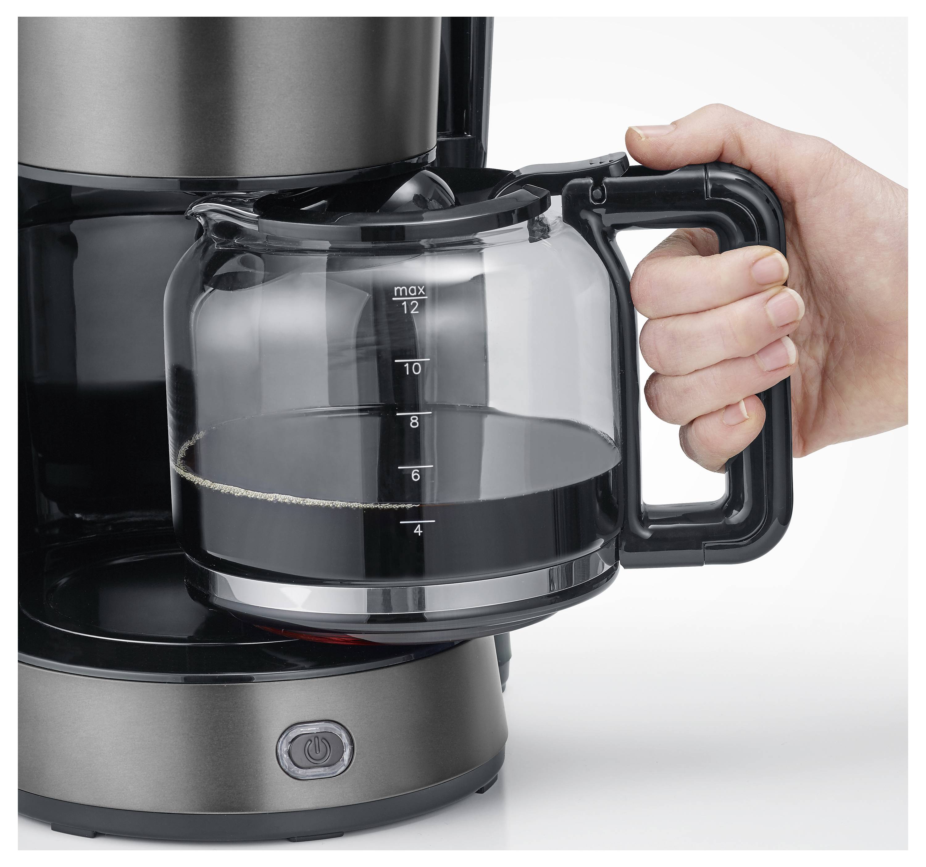 Eine Hand hält eine Glaskaffeekanne, zur Hälfte mit Kaffee gefüllt, vor einer Kaffeemaschine. Das "max"-Etikett zeigt die Kapazität von 12 Tassen an.