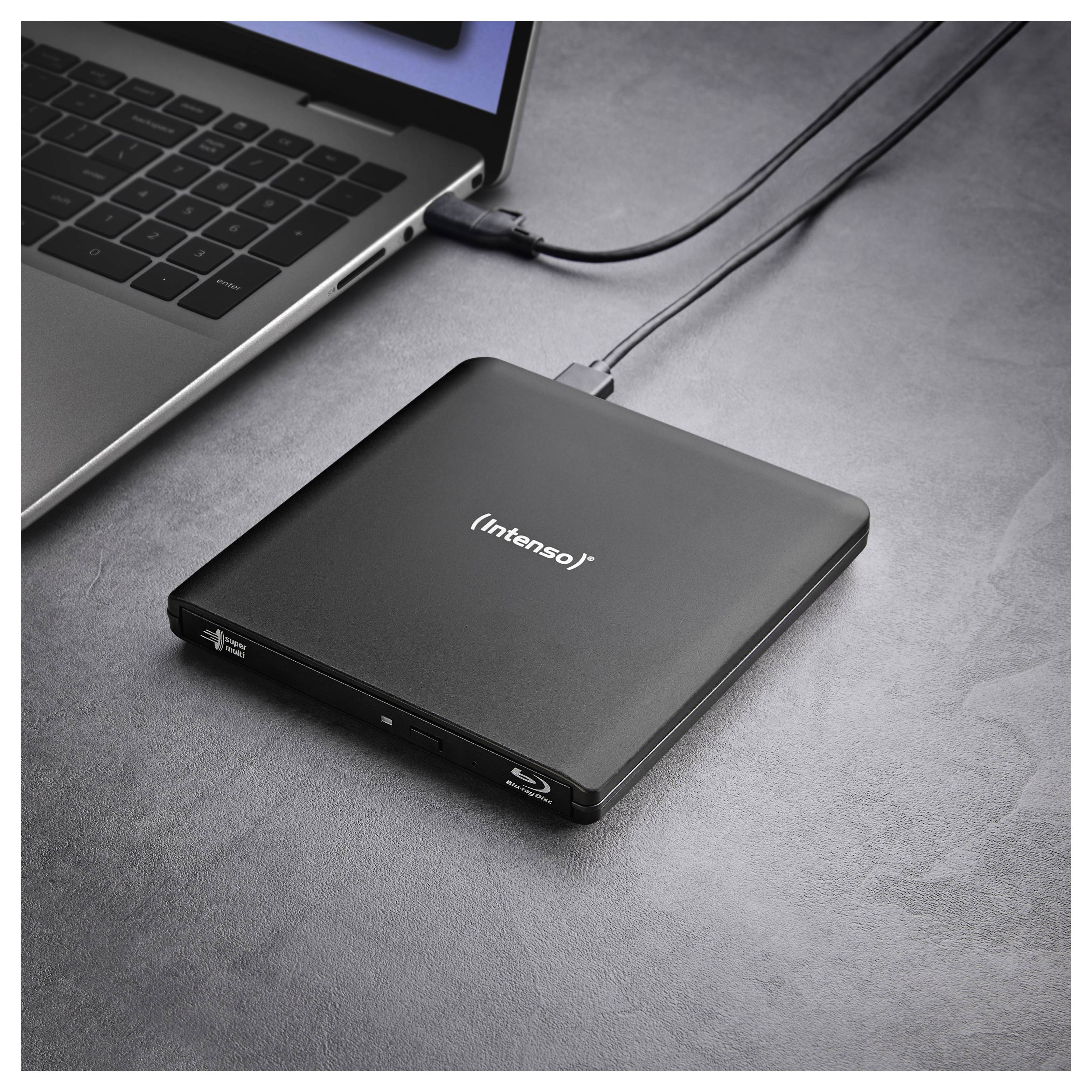 Ein externes optisches Laufwerk, das über USB mit einem Laptop verbunden ist, auf einer grauen Oberfläche platziert.