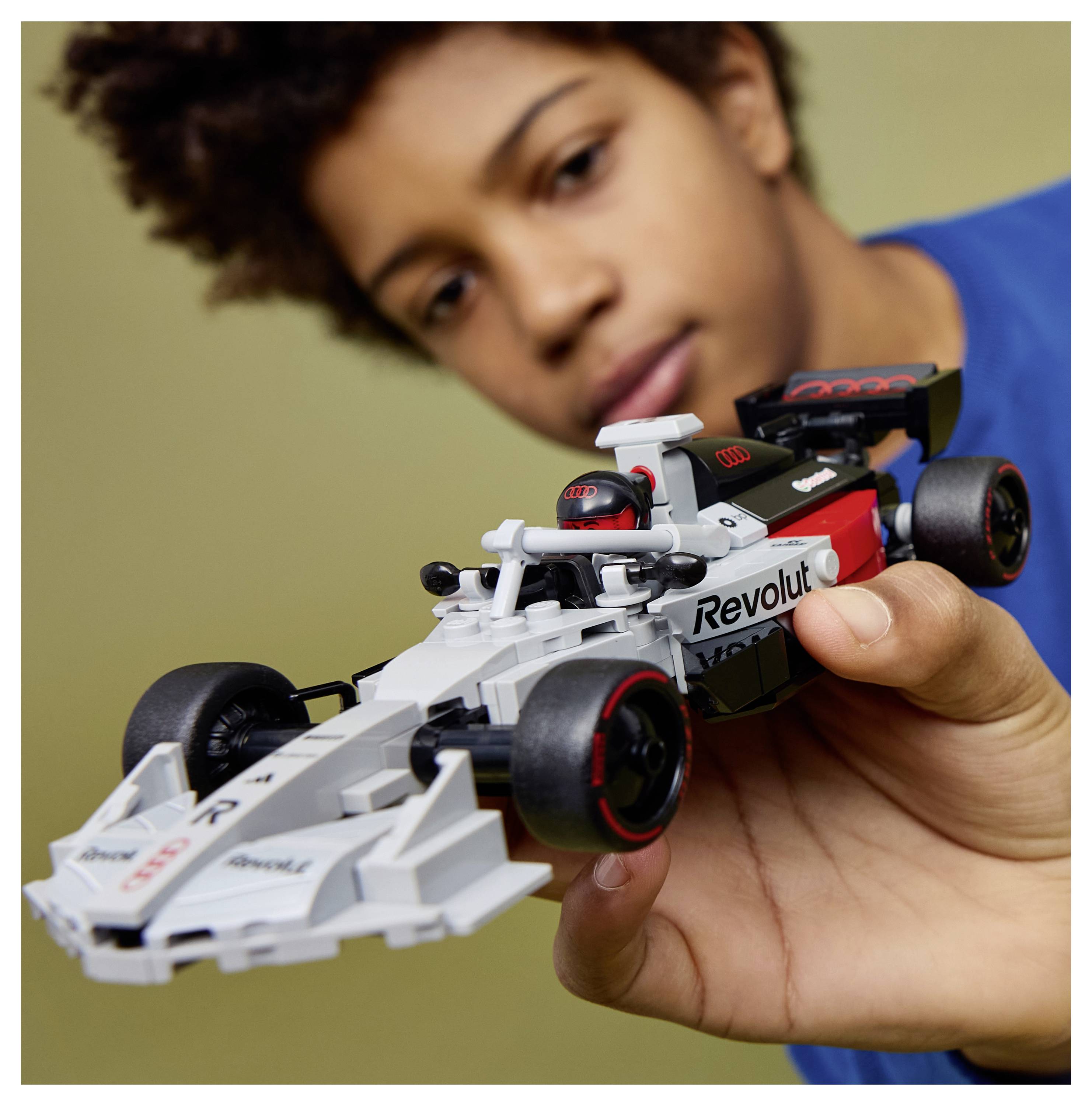 Eine Person hält ein detailliertes Spielzeug-Rennwagen-Modell mit dem Wort "Revolut" darauf und zeigt damit Interesse an Rennsport oder Modellautos.