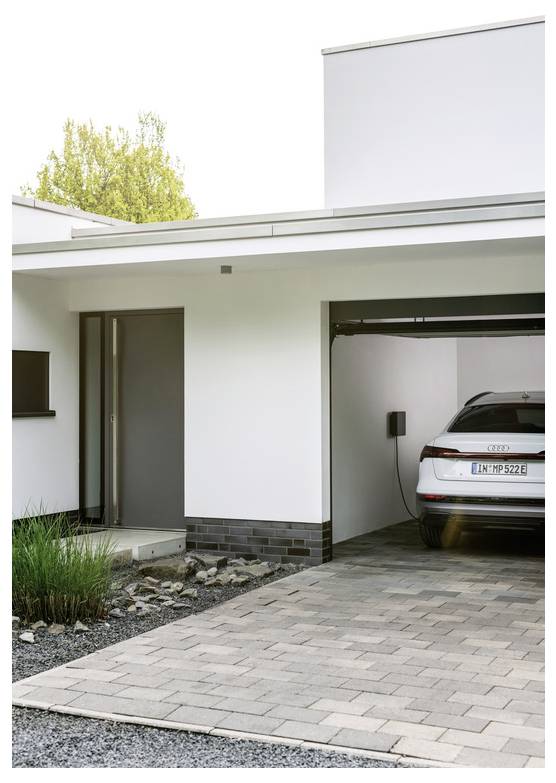 Modernes weißes Haus mit einer Einfahrt, die zu einer Garage führt, in der ein Audi-SUV geparkt ist und offenbar aufgeladen wird.