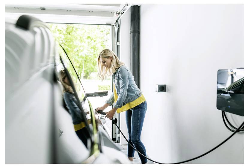 Eine Frau lädt ein Elektroauto in einer Garage auf und steckt das Kabel in das Fahrzeug neben einer offenen Tür.