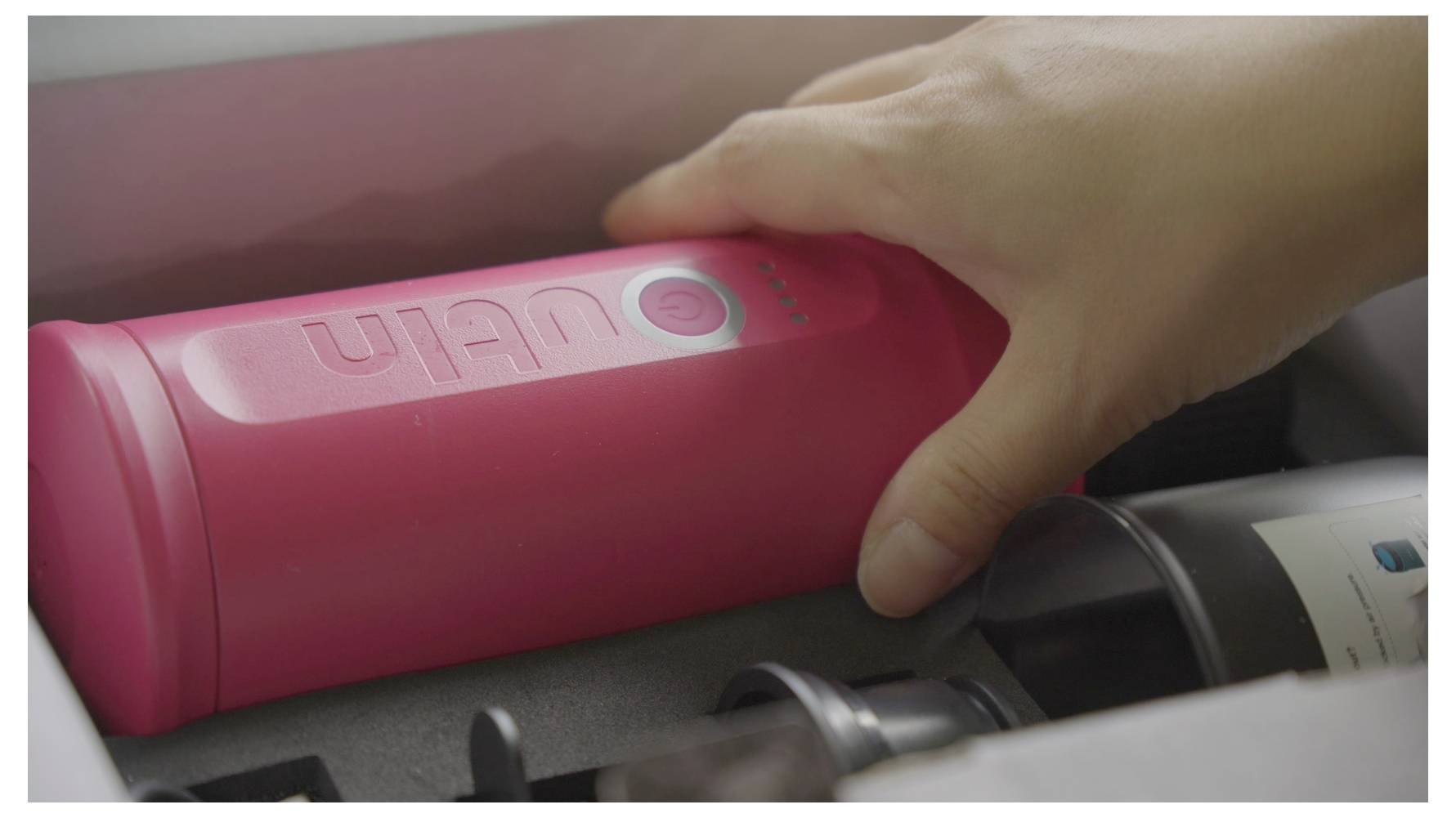 Eine Person, die nach einem rosa zylindrischen Objekt greift, das mit „Ulan" beschriftet ist und in einer schaumstoffgepolsterten Box mit anderen Gegenständen platziert ist.
