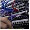 Eine Person verbindet ein schwarzes Netzwerkkabel mit der Bezeichnung „AD05-10-01" mit einem Serverrack, das mit verschiedenfarbigen Kabeln und Schaltern gefüllt ist.
