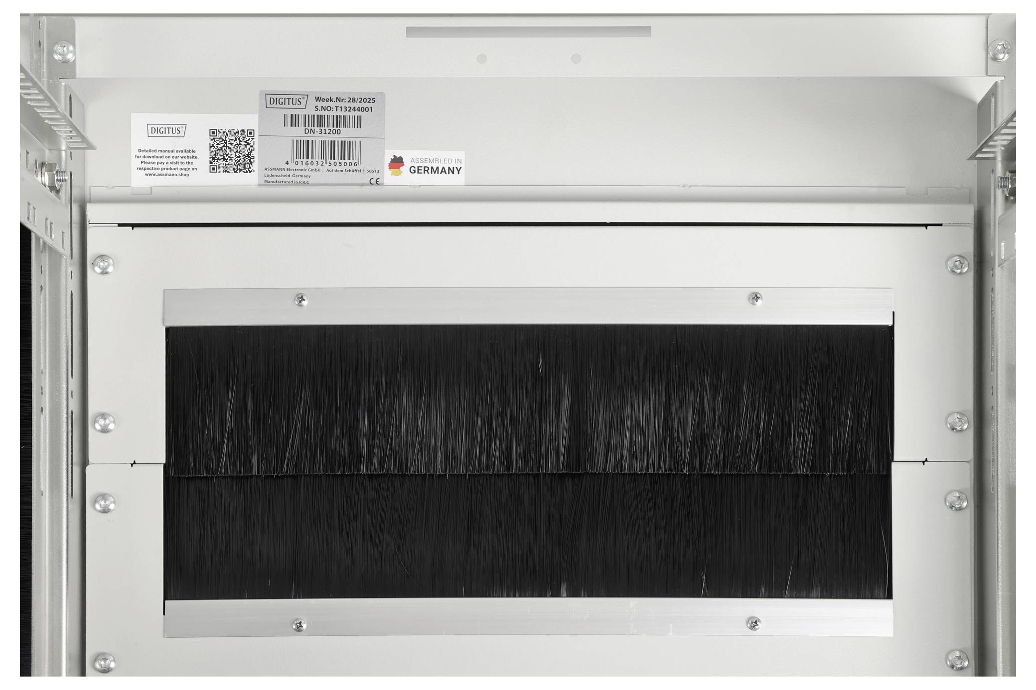 Ein weißer Schrank mit einem Barcode und einem Aufkleber mit deutscher Flagge oben, mit einer großen rechteckigen Öffnung, die mit schwarzen Borsten bedeckt ist.