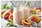 Zwei Pfirsich-Smoothies in Gläsern mit gestreiften Strohhalmen sind umgeben von frischen Pfirsichen und Blättern auf einem hellen Stoff.