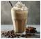 Ein cremiger Eiskaffee mit Schlagsahne und Zimt obenauf, umgeben von verstreuten Kaffeebohnen und Schokoladenkeksen auf einem Tisch.